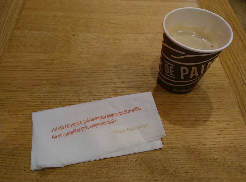 Un café y una servilleta con un mensaje escrito en francés que pide que no la desperdicies.